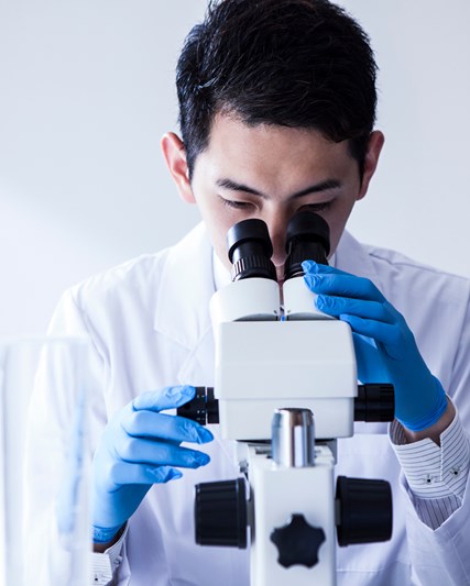 Male employee in lab, using microscope 