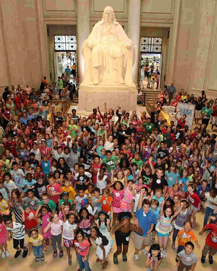 Lots of children inside a large historical building with a statue