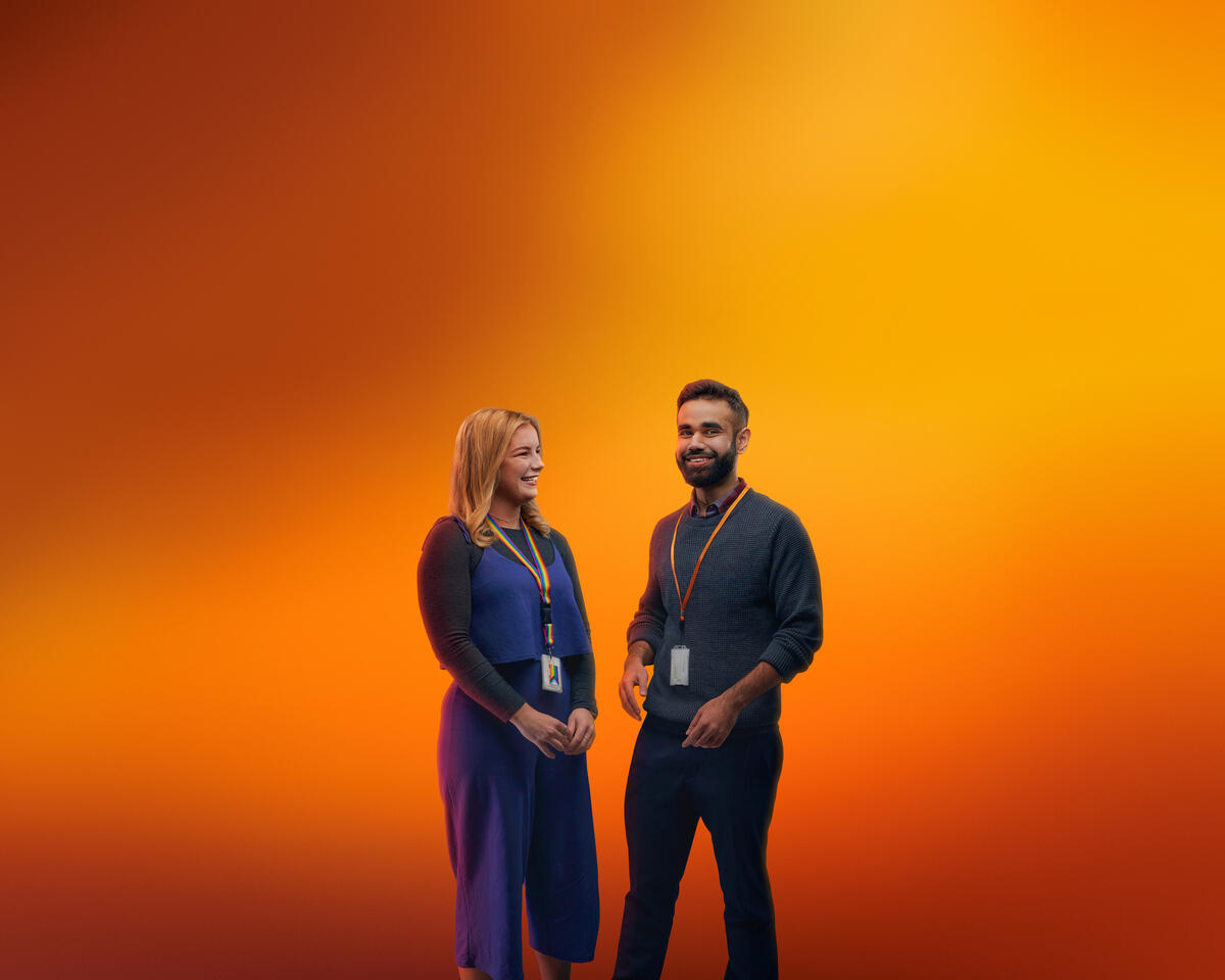 Duas pessoas com badges da GSK, fotografadas em fundo laranja