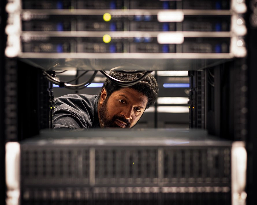 Técnico a trabalhar no interior de um rack de servidores, ajustando cabos e equipamentos de rede num centro de dados